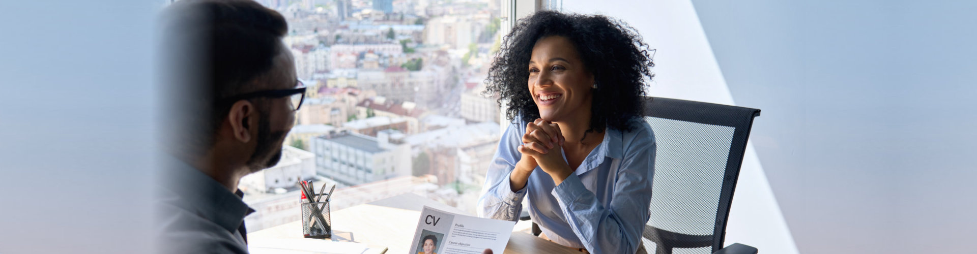 Friendly interview between Indian businessman hr director holding paper cv hiring for job female African American applicant manager sitting in contemporary office. Human resources recruitment concept.